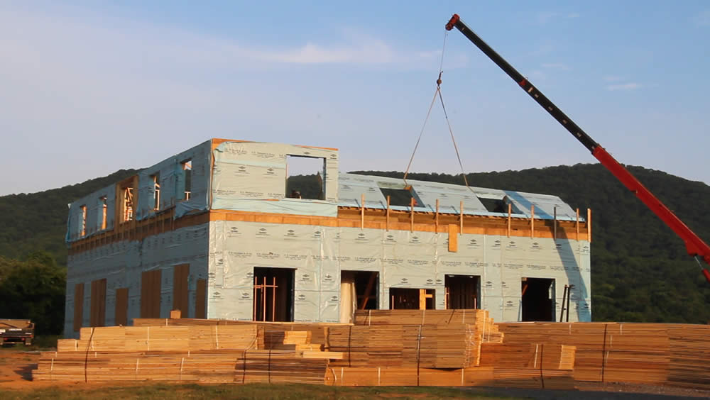JUNE 13 - Crane raises remaining east wall panel as workers push and position from behind.  Bundles of roof trusses can be seen in front of temple.