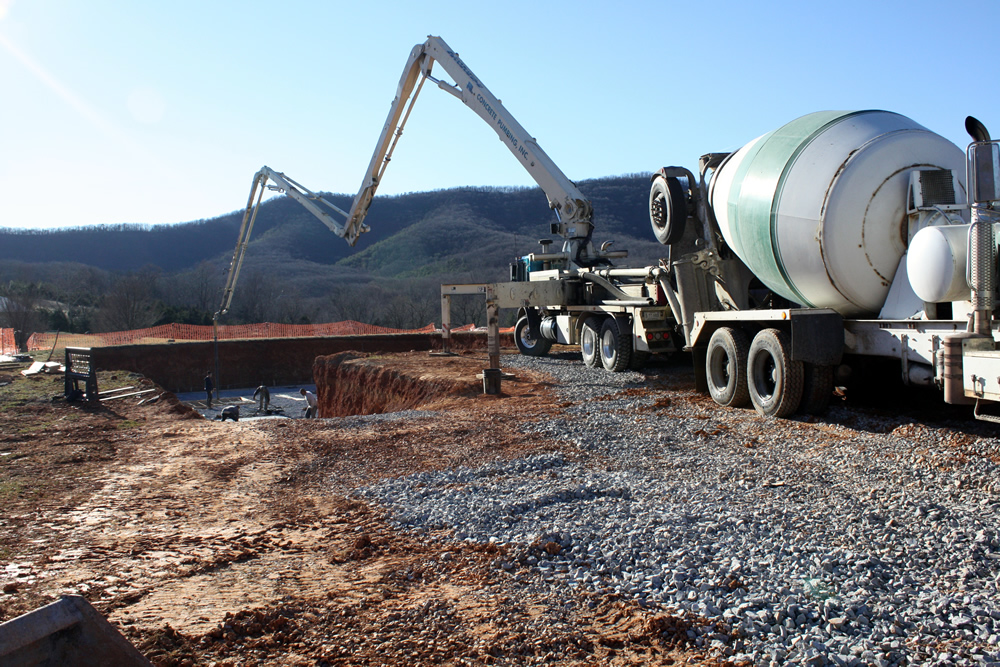 The concrete pumping truck pumping cement from the cement mixer as workers guide hose to the necessary locations.