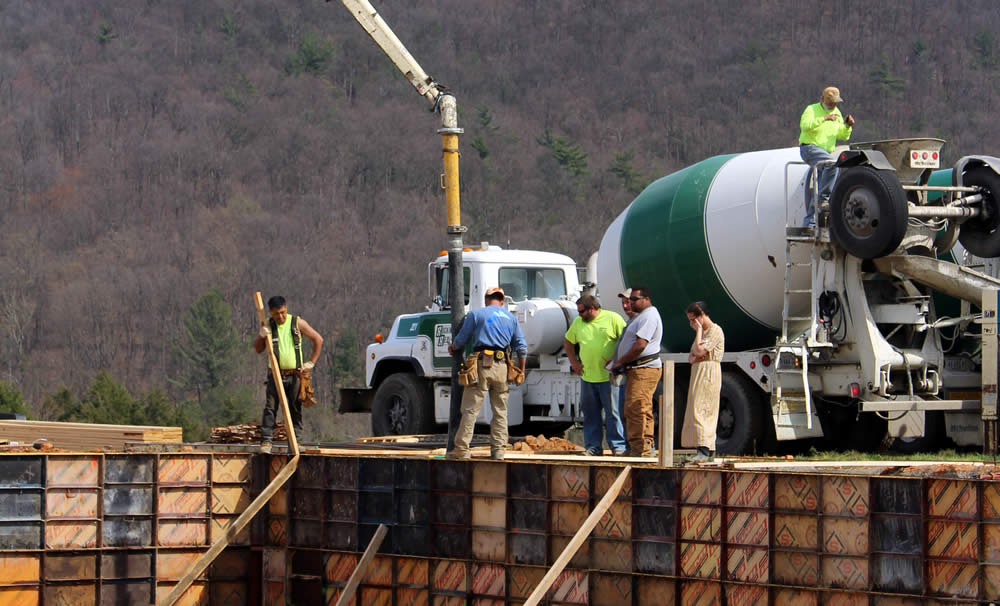 View of workers pumping concrete into wall-forms. 25 cement mixer loads of concrete were required to create the foundation walls!