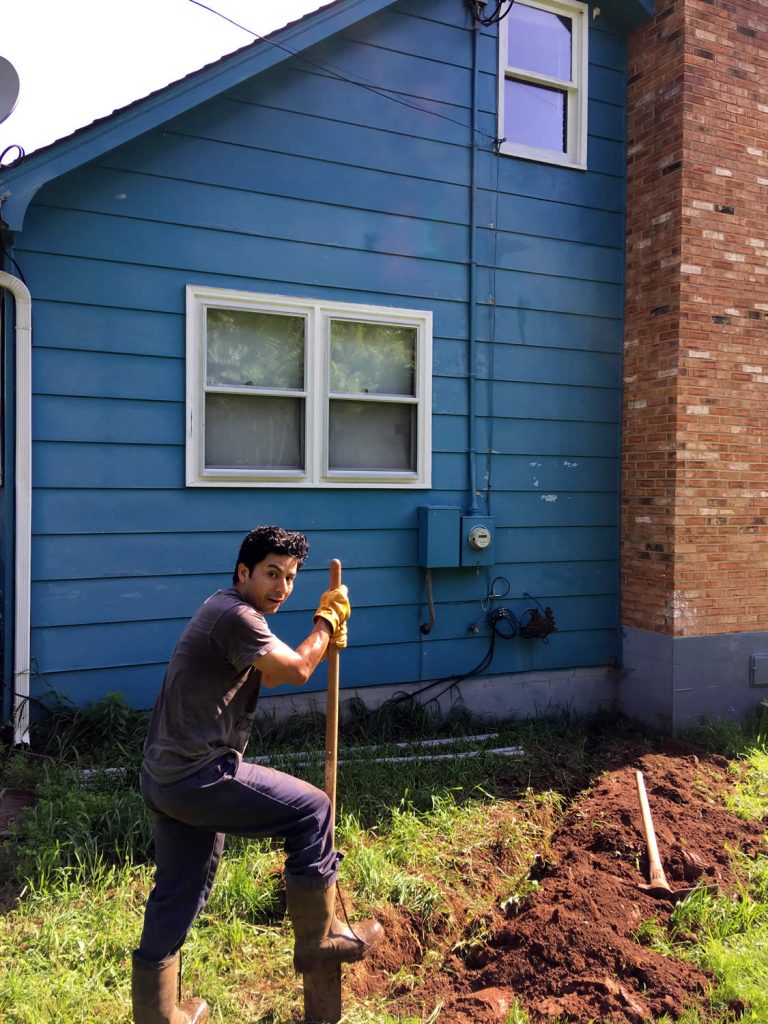 Jessie Hercules digs a trench for underground conduit which will carry the cat6 cable into the Blue House from the nearest hand-hole.