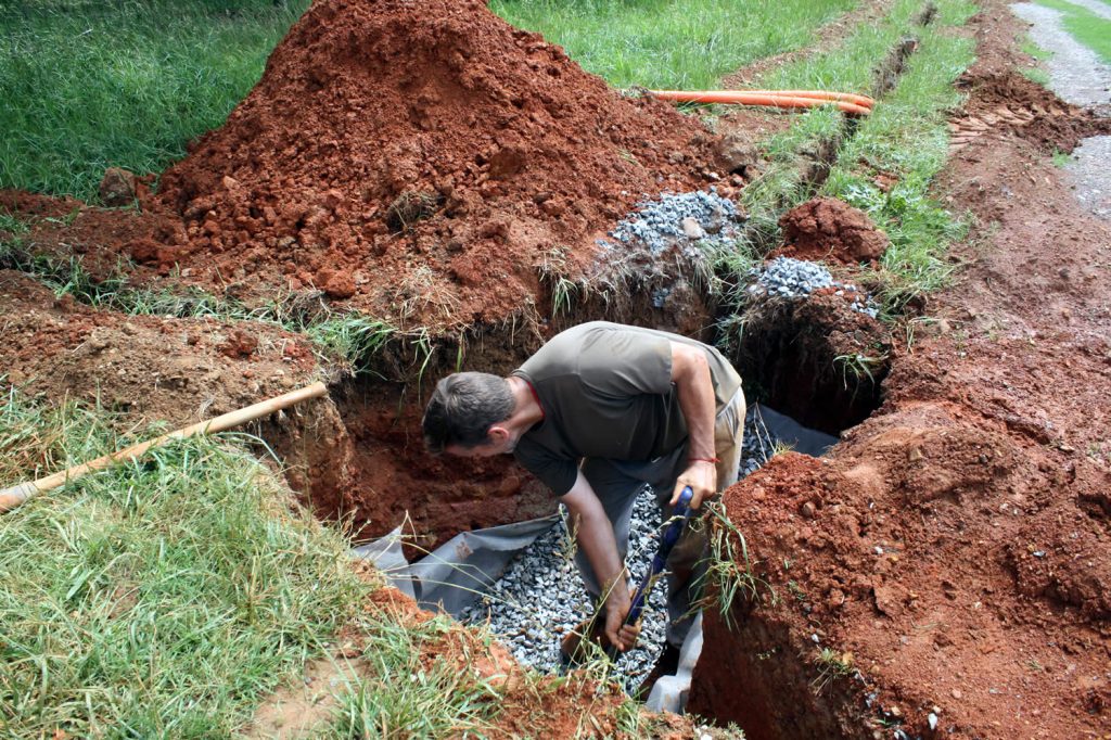 Dean Baker shovels gravel to help with drainage around the hand-hole.